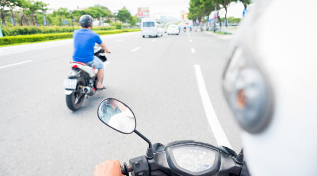 Da Nang, Vietnam - May 7, 2018: a man in helmet drives a motorbike on a highway, a view from the behind the driver.

White helmet, a hand, motorbike's dashboard and the street with another scooter (blurred) going ahead towards other traffic. Traveling by motor bike taxi